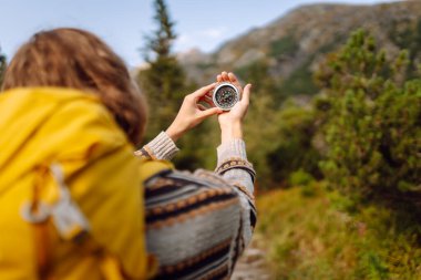 Sarı sırt çantalı kadın yürüyüşçünün dağ manzarasına pusula tutuşu. Pusula ile yön arayan ve vahşi doğayı keşfeden genç bir kadın. Doğa konsepti, navigasyon.