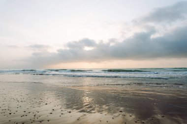 Deniz Burnu. Güneş arka planda batarken kumlu bir sahile yumuşak dalgalar vuruyor. Huzurlu bir manzara. Vahşi yaşam konsepti.