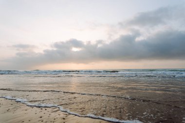 Deniz Burnu. Güneş arka planda batarken kumlu bir sahile yumuşak dalgalar vuruyor. Huzurlu bir manzara. Vahşi yaşam konsepti.