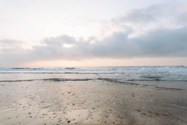 Deniz Burnu. Güneş arka planda batarken kumlu bir sahile yumuşak dalgalar vuruyor. Huzurlu bir manzara. Vahşi yaşam konsepti.