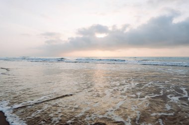 Deniz Burnu. Güneş arka planda batarken kumlu bir sahile yumuşak dalgalar vuruyor. Huzurlu bir manzara. Vahşi yaşam konsepti.