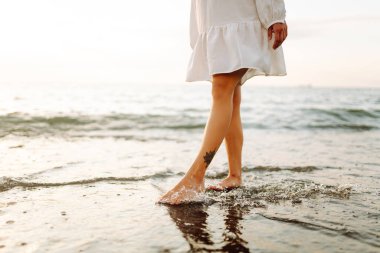 Gün batımında sahilde yürüyen bir kadının bacaklarının yakın çekimi. Genç bir kadın deniz manzarasının tadını çıkarıyor, sahilde yürüyor. Doğa, rahatlama konsepti.