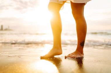 Gün batımında sahilde yürüyen bir kadının bacaklarının yakın çekimi. Genç bir kadın deniz manzarasının tadını çıkarıyor, sahilde yürüyor. Doğa, rahatlama konsepti.