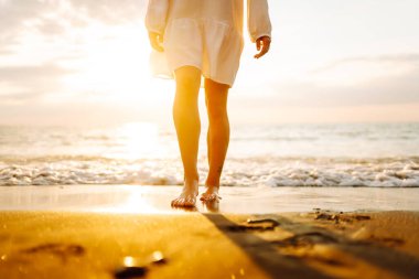 Gün batımında sahilde yürüyen bir kadının bacaklarının yakın çekimi. Genç bir kadın deniz manzarasının tadını çıkarıyor, sahilde yürüyor. Doğa, rahatlama konsepti.