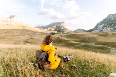 Sırt çantalı, parlak sarı yağmurluklu neşeli bir kadın dağ manzarasının tadını çıkarıyor. Bir yürüyüşçü dağ yolunda yürürken kendini özgür hisseder. Etkin yaşam biçimi.