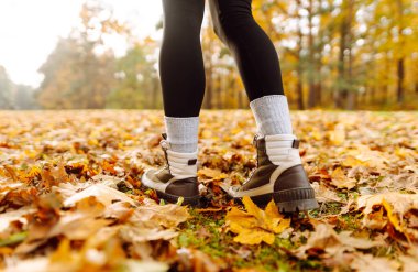 Yürüyüş botlarıyla bir yürüyüşçünün ayaklarının yakın çekimi sarı yapraklarla kaplı bir patika boyunca yürüyor. Ağır çizmeli bir kadın ormanda sonbahar gününün tadını çıkarır. Yürüme, yürüyüş kavramı. Sonbahar günü!