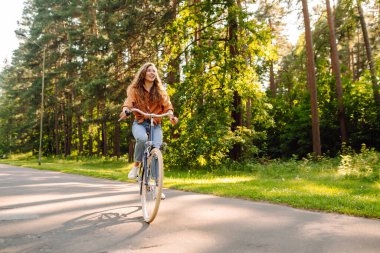 Neşeli bir kadın güneşli bir ormanda bisiklet sürüyor. Güzel bir kadın doğal çevreden zevk alır ve gün batımında bisiklete biner. Hafta sonu ve eğlence konsepti.