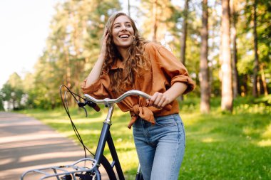 Neşeli bir kadın güneşli bir ormanda bisiklet sürüyor. Güzel bir kadın doğal çevreden zevk alır ve gün batımında bisiklete biner. Hafta sonu ve eğlence konsepti.
