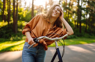 Neşeli bir kadın güneşli bir ormanda bisiklet sürüyor. Güzel bir kadın doğal çevreden zevk alır ve gün batımında bisiklete biner. Hafta sonu ve eğlence konsepti.