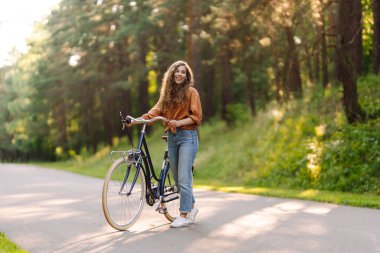 Neşeli bir kadın güneşli bir ormanda bisiklet sürüyor. Güzel bir kadın doğal çevreden zevk alır ve gün batımında bisiklete biner. Hafta sonu ve eğlence konsepti.