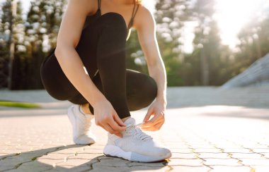 Yakın plan: Spor ayakkabılı genç bir atlet ayakkabı bağcıklarını spor sahasında bağlıyor. Spor ayakkabılı bir kadın dışarıda antrenman yapıyor. Spor ve antrenman konsepti. Etkin yaşam biçimi.