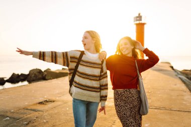 İki genç kadın gün batımı rıhtımında eğleniyorlar. Kız arkadaşları arka planda bir deniz feneriyle vakit geçiriyorlar. Arkadaşlık kavramları, yürüme. Etkin yaşam biçimi.