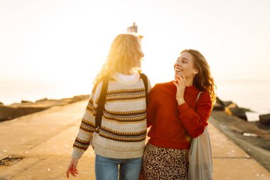 İki genç kadın gün batımı rıhtımında eğleniyorlar. Kız arkadaşları arka planda bir deniz feneriyle vakit geçiriyorlar. Arkadaşlık kavramları, yürüme. Etkin yaşam biçimi.