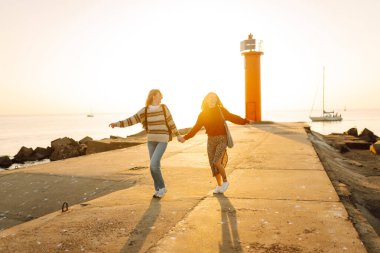 İki genç kadın gün batımı rıhtımında eğleniyorlar. Kız arkadaşları arka planda bir deniz feneriyle vakit geçiriyorlar. Arkadaşlık kavramları, yürüme. Etkin yaşam biçimi.