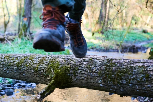person in boots jumping on broken tree trunk in forest above river