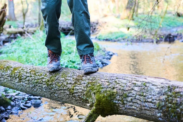 person in boots walking on broken tree trunk in forest above river