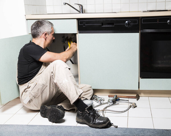 specialist male plumber repairs faucet in kitchen
