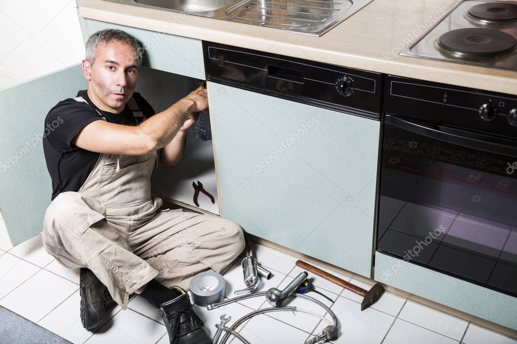 specialist male plumber repairs faucet in kitchen