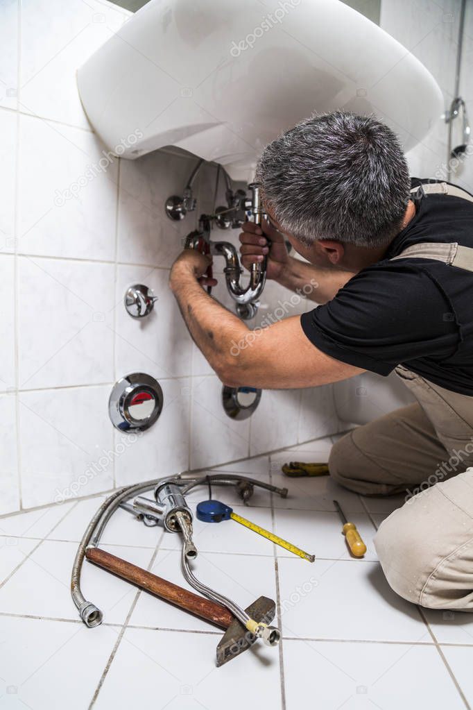 specialist male plumber repairs faucet in bathroom