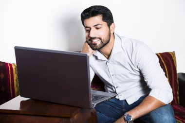 Bilgisayarda çalışarak rahat kıyafetler içinde oturan adam.