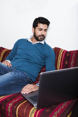 Bilgisayarda çalışarak rahat kıyafetler içinde oturan adam.