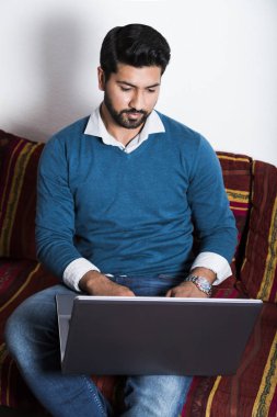 Bilgisayarda çalışarak rahat kıyafetler içinde oturan adam.