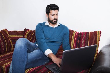 Bilgisayarda çalışarak rahat kıyafetler içinde oturan adam.