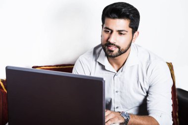 Bilgisayarda çalışarak rahat kıyafetler içinde oturan adam.