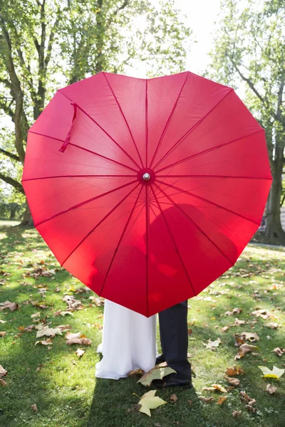 Nászutas pár piros szív alakú napernyő árnyékában körvonalai — Stock Fotó