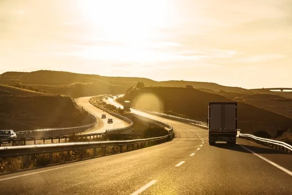 Lastbil og biler kører på motorvej ved solnedgang - Stock-foto
