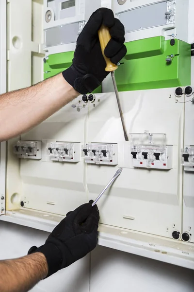 Electrician repairs with screwdriver distribution board close up