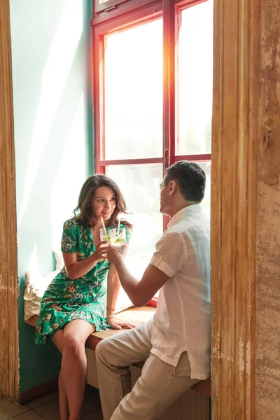 Hermosa pareja sentada en el alféizar de la ventana con cócteles —  Fotos de Stock