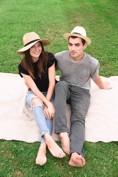 Junges positives Paar sitzt zusammen auf Strohhüten — Stockfoto