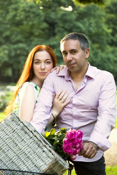 Ehepaar trägt Picknickkorb und Rosen mit dem Fahrrad — Stockfoto