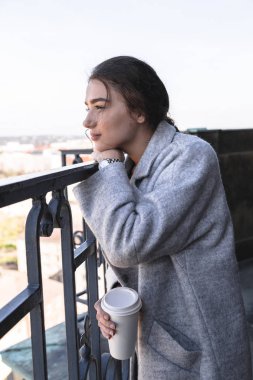 Kız elinde kahve fincan ile balkonda duruyor