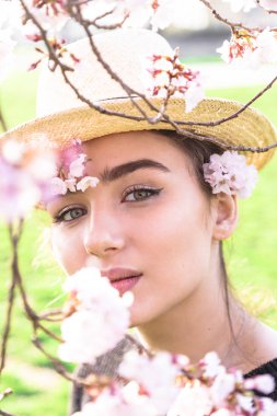 Hasır şapkalı kız çiçekli dalı arkasına saklandı