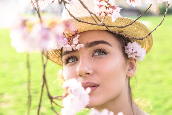 Дівчина в солом'яному капелюсі мрійливо дивиться на розквітлу гілку — стокове фото