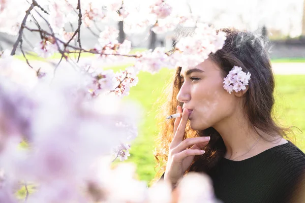 Chica se para de lado y fuma cerca de árbol al aire libre — Foto de Stock