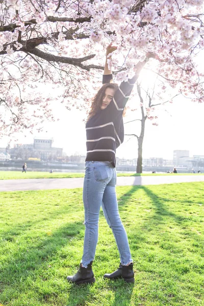 Девушка стоит рядом с цветущим деревом и поднимает руки — стоковое фото