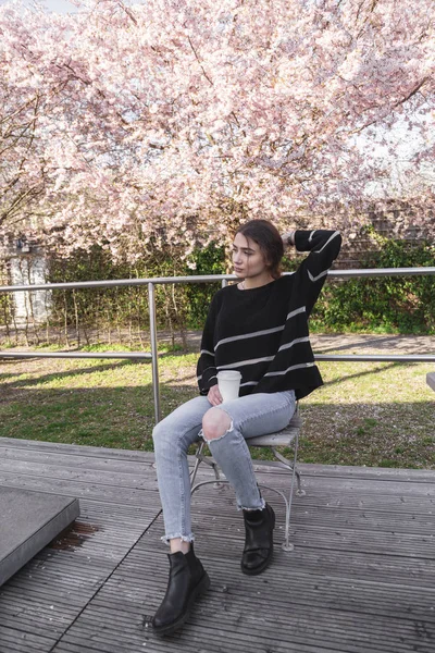 Девушка сидит на цветущем дереве, прикасается к волосам — стоковое фото
