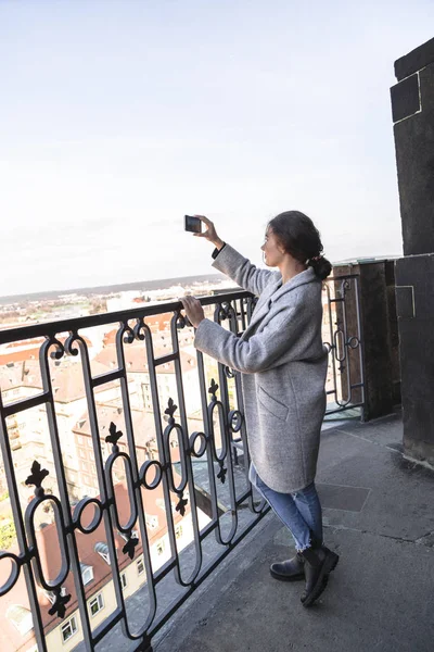 Девушка фотографирует городской пейзаж, стоящий на балконе — стоковое фото