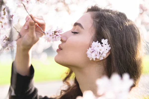 Chica sonríe y huele flores en rama de flor — Foto de Stock
