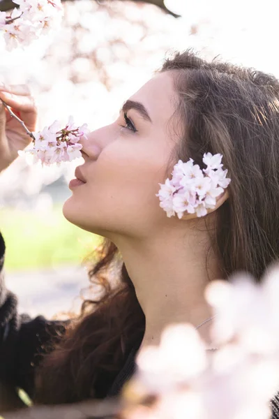 Chica sonríe y huele flores en rama de flor — Foto de Stock