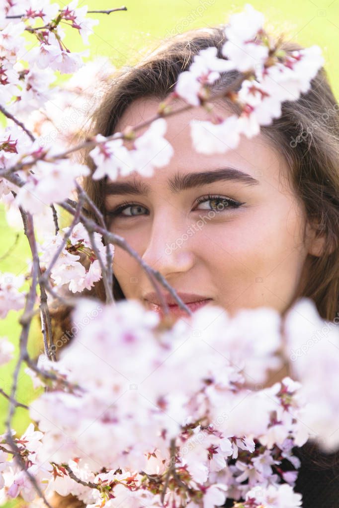 Girl hids behind flowering branch of blooming tree