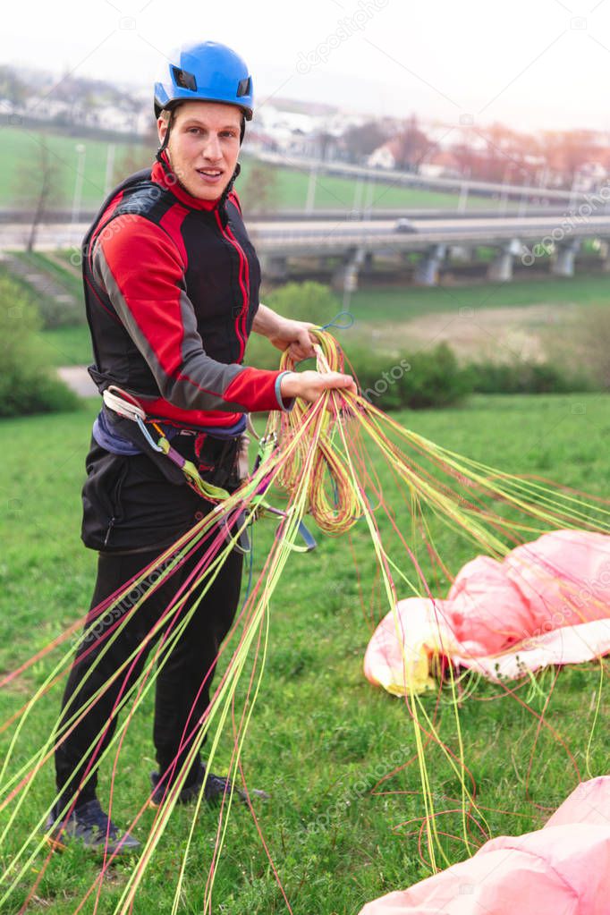 Landed young male paraglider raises parachute from ground