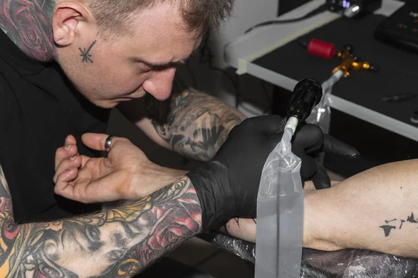 Майстер нахиляється над рукою чоловіка і робить татуювання на ньому — стокове фото