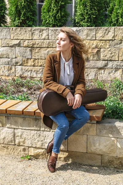 Молодая женщина со скрипкой сидит на деревянной скамейке — стоковое фото