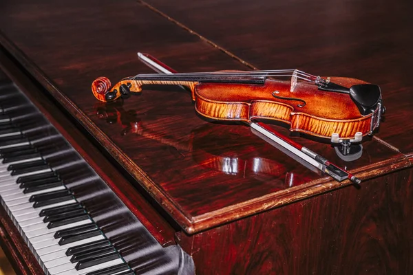 Violin with bow lying on piano on brown background — Stock Photo, Image
