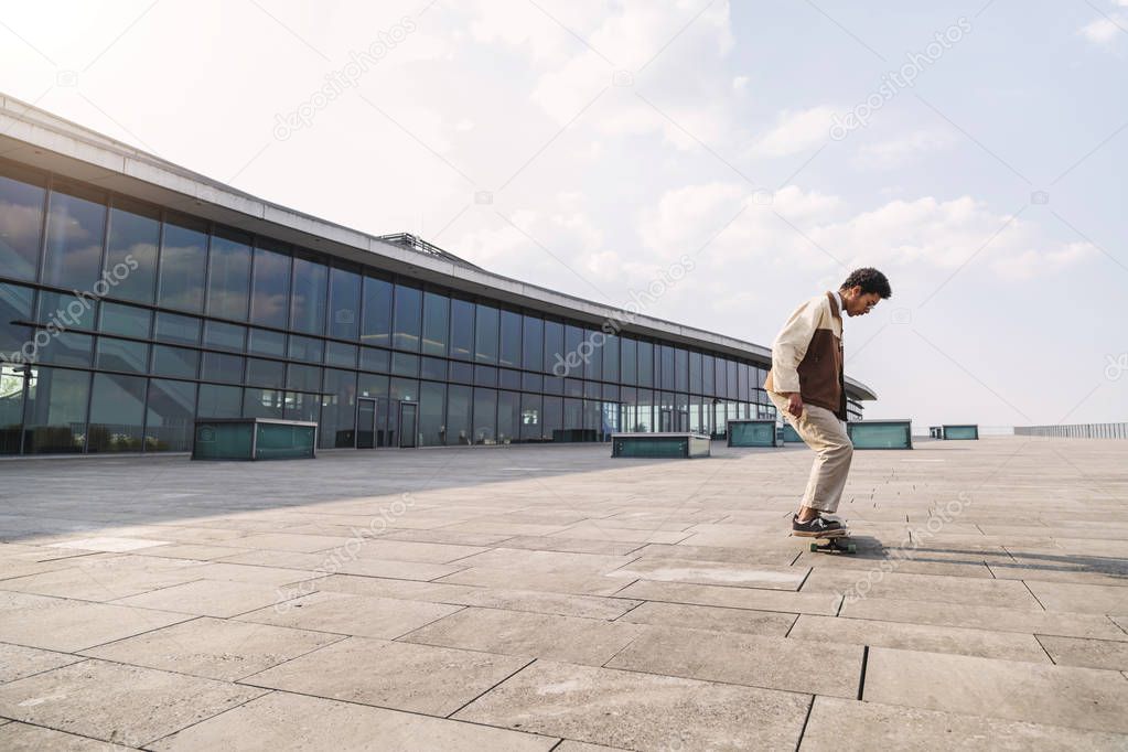 Afro guy gliding on his skateboard on stone square