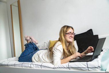 Dizüstü bilgisayarda çalışan gülümseyen kız, yatağında yatıyor